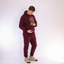 Man in Red Burgundy hoodie and pants holding a small dog on a white background