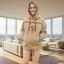 Person wearing a beige boucle hoodie with a dog design, standing in a room with a couch and window.