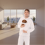 Person wearing a white hoodie with small dog inside on a light pink background