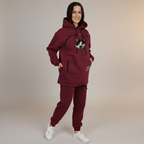 Person wearing a burgundy tracksuit with a cat in pouch against a beige background