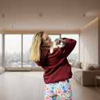 Woman in a  Burgundy hoodie holding a cat in the living room