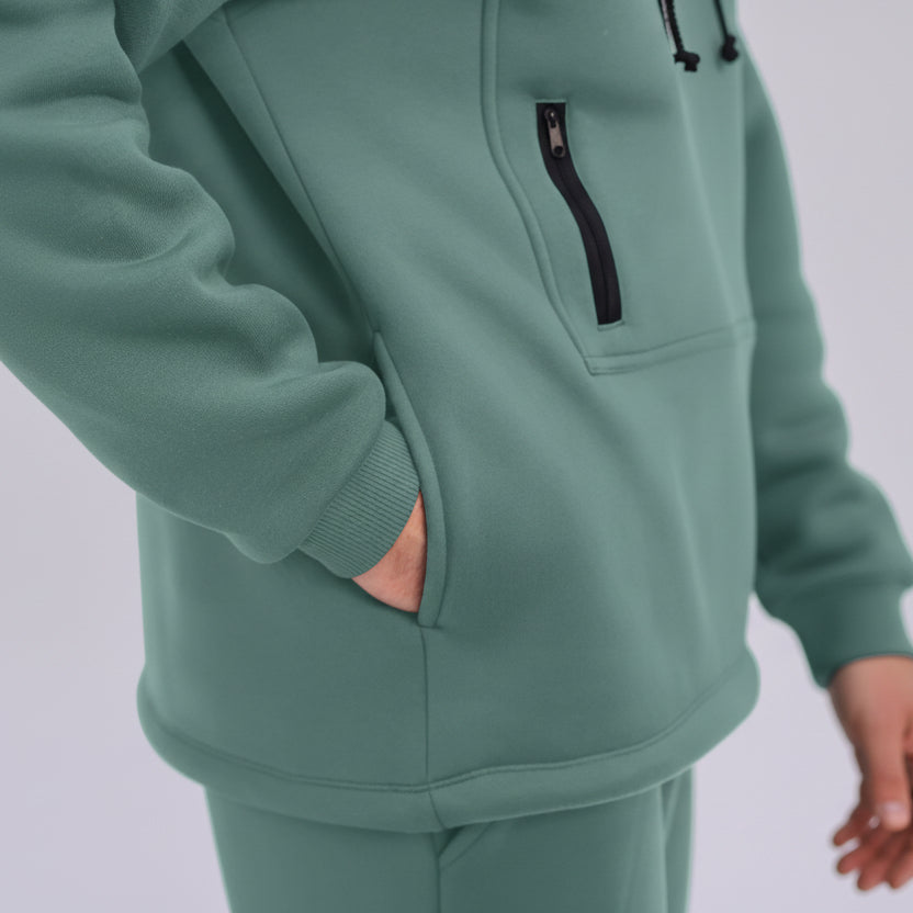 Emerald Green tracksuit with a focus on the jacket's pocket and zipper on a light purple background