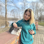 Woman in teal jacket with a cat on a bench outdoors
