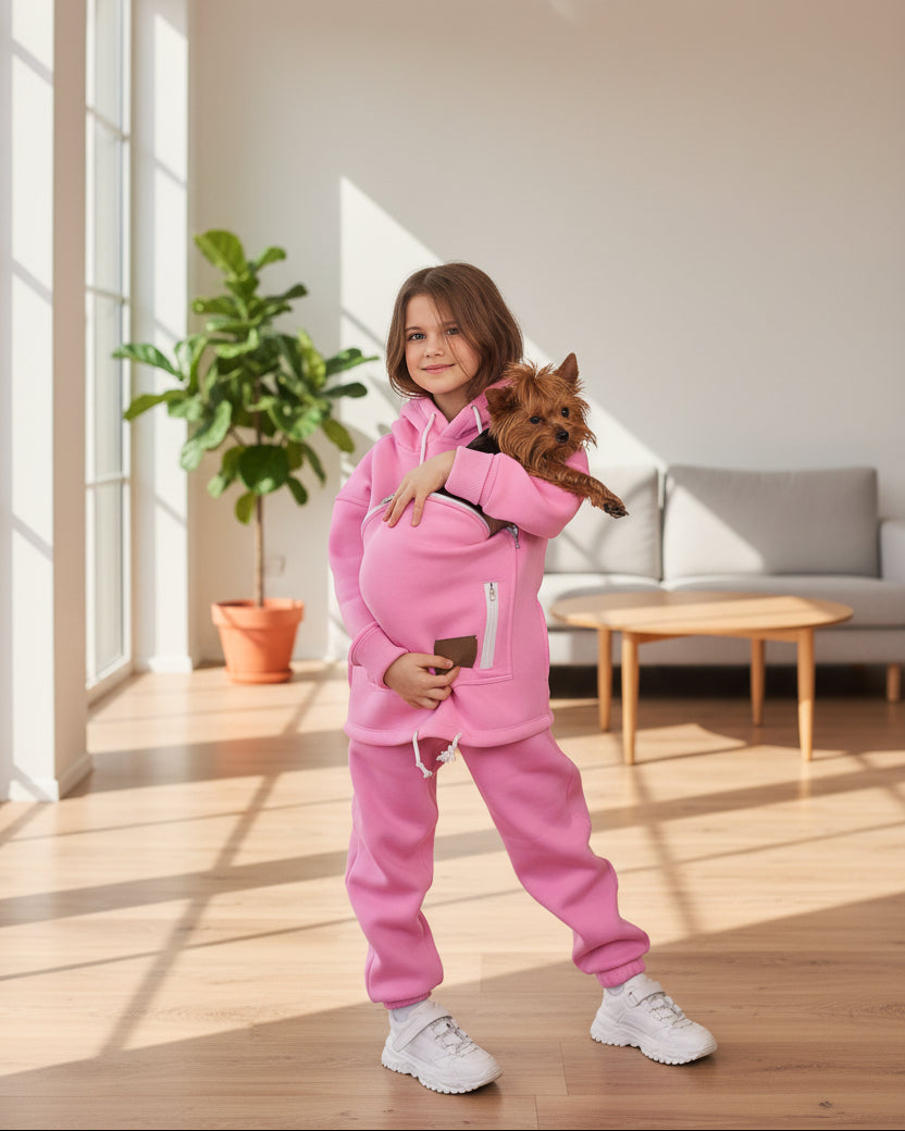 Child in pink outfit holding a small dog in a bright living room.