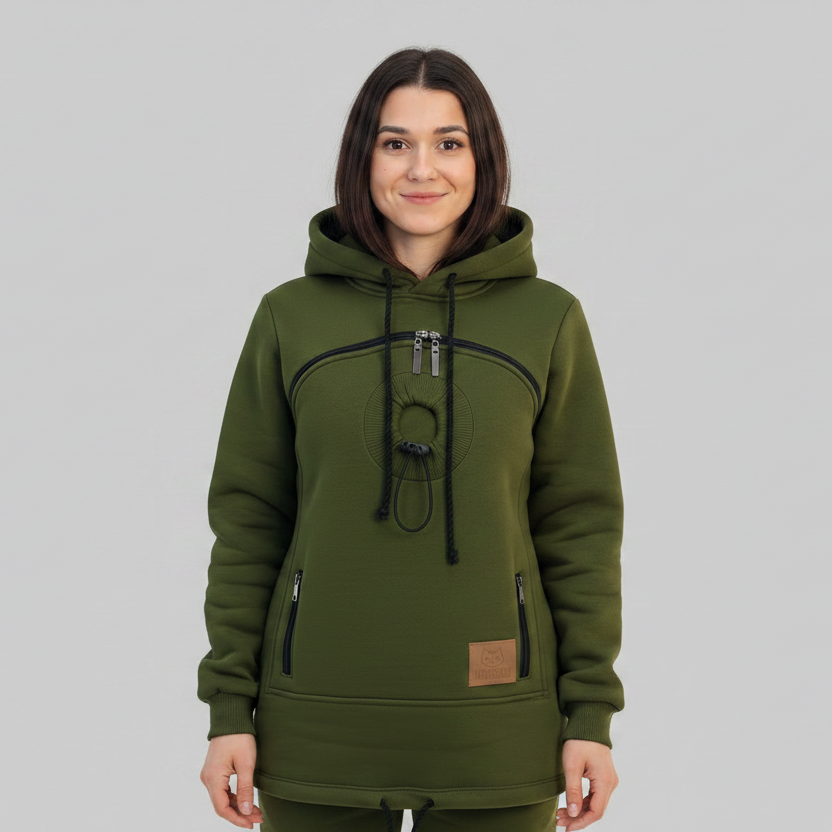 A woman wearing an dark green hooded sweatshirt with black drawstrings and a circular graphic print on the chest, standing against a solid gray studio background.