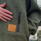 Khaki Sherpa fleece jacket with a brand patch and zipper, blurred background