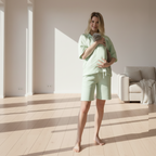 Woman in lime green outfit holding a cat in a sunlit room.