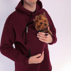 Person wearing a Red Burgundy hoodie holding a small brown dog.