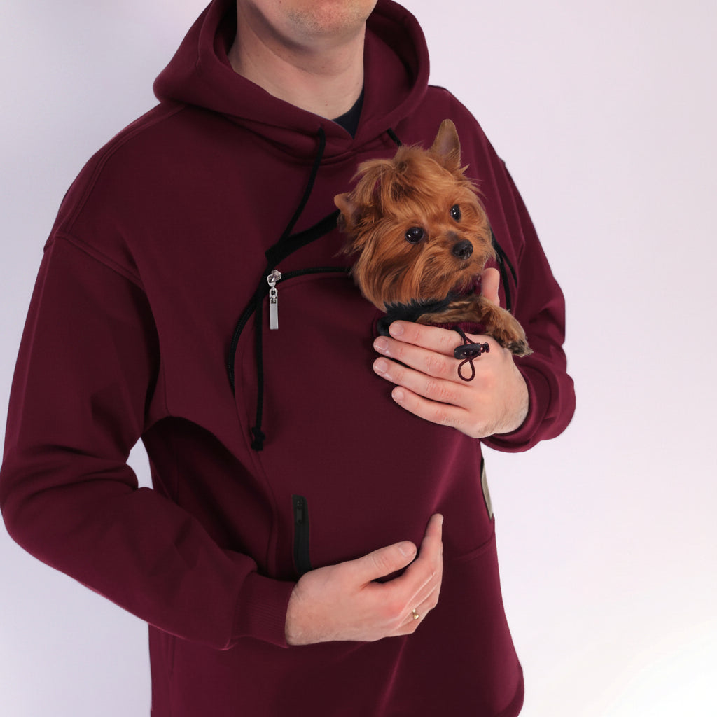 Person wearing a Red Burgundy hoodie holding a small brown dog.