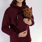 Person wearing a burgundy hoodie with a small dog inside, on a white background