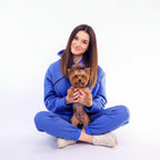 Woman in Royal Blue tracksuit holding a small brown dog on a white background