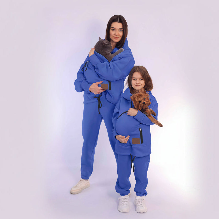 Two people in matching Royal Blue outfits holding small dogs on a white background