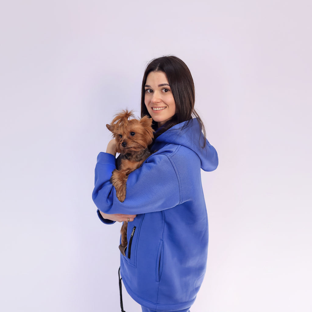 Woman in a Royal Blue jacket holding a small brown dog on a white background