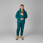 Man wearing teal outdoor gear holding a small dog on a gray background