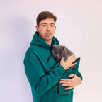 Man in teal hoodie holding a gray cat against a white background