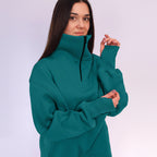 Woman wearing a teal sweatshirt with a high collar on a white background