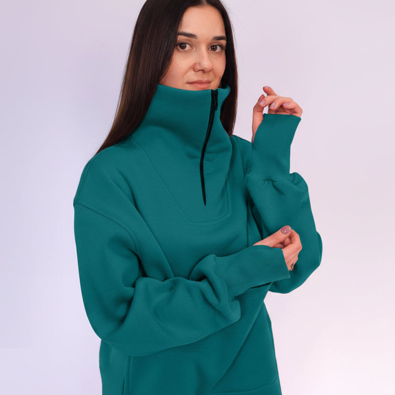 Woman wearing a teal sweatshirt with a high collar on a white background