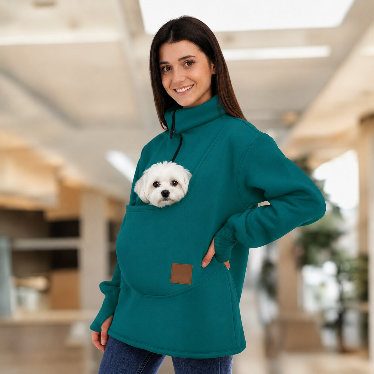 Women wearing a teal sweatshirt with a dog in pouch, standing indoors.