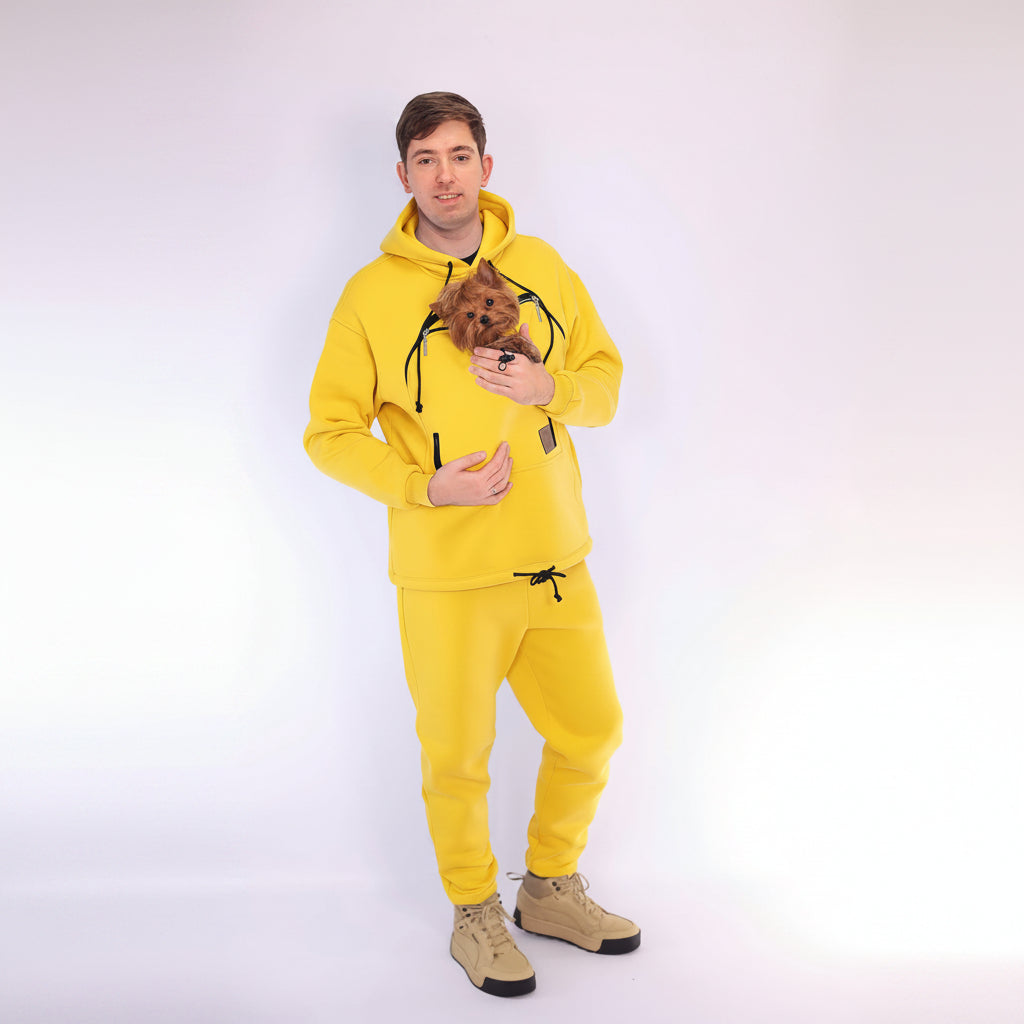 Men wearing a yellow hoodie and matching pants holding a small dog on a white background
