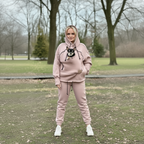 Person wearing a beige hoodie with a dog and matching pants in a park.