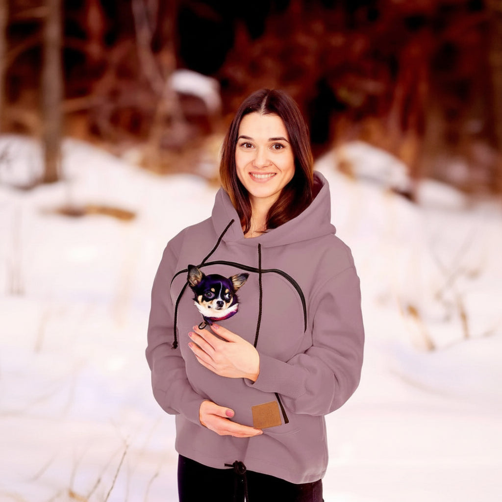 Woman wearing a beige hoodie with a small dog plush toy in a snowy outdoor setting
