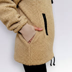 Beige sherpa hoodie with a hand peeking out from a pocket on a white background