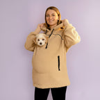 Person wearing a beige boucle fleece hoodie with a small dog peeking out from inside, against a light purple background