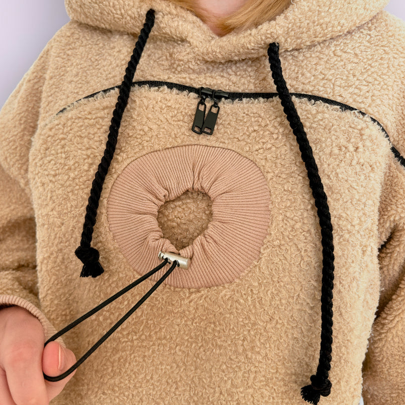 Close-up of a beige boucle fleece hoodie with black drawstrings and a heart design on the chest.