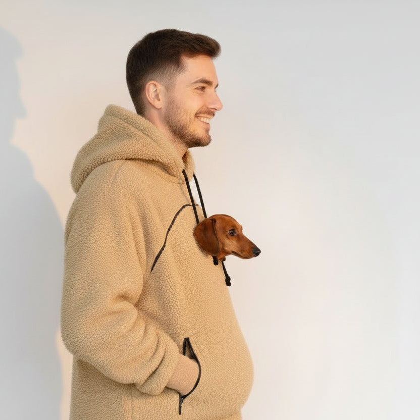 Man wearing a beige fleece hoodie with a small dog peeking out from inside, on a plain background