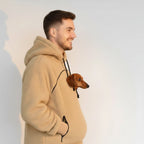 Man wearing a beige fleece hoodie with a small dog peeking out from inside, on a plain background