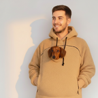 Man wearing a beige boucle hoodie with a small dog peeking out from under the hood against a plain background