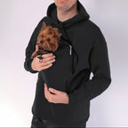 Person wearing a black hoodie holding a small brown dog.