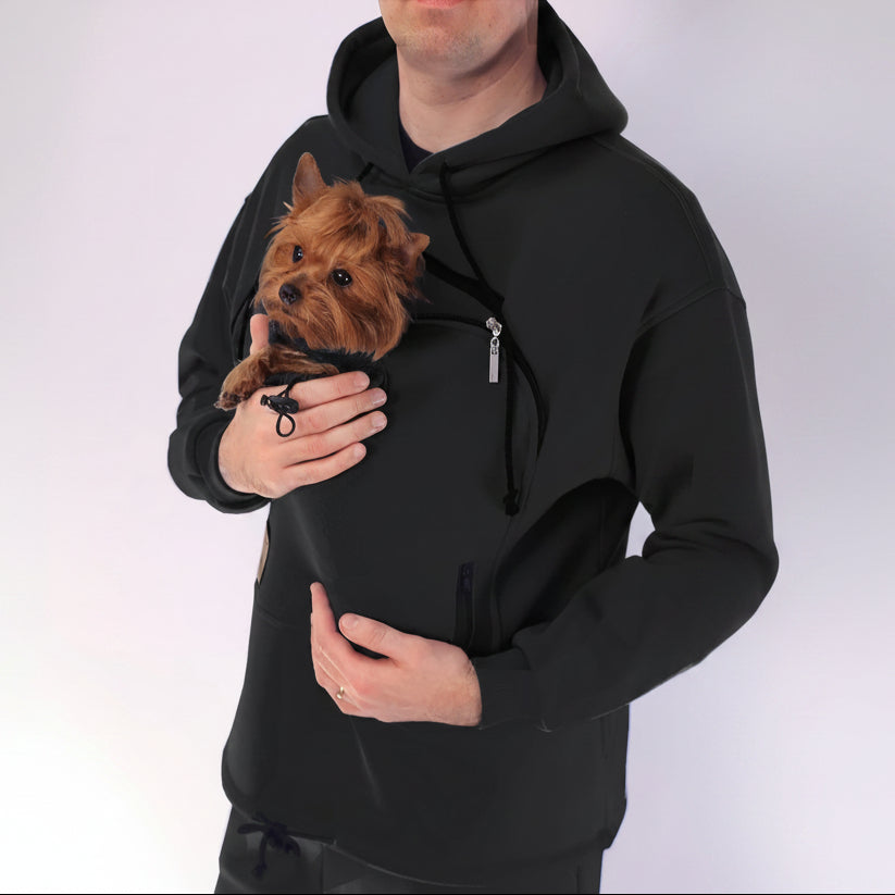 Person wearing a black hoodie holding a small brown dog.