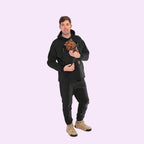 Man wearing a black hoodie with a dog inside, standing against a white background