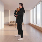 Woman in black tracksuit holding a small dog in a white room with plants.