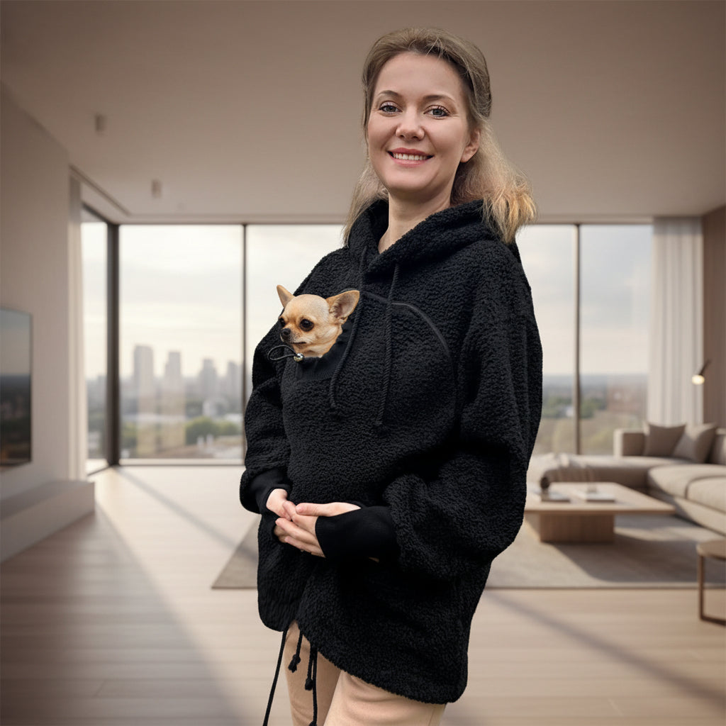 Woman holding a small dog in a black boucle hoodie in living room