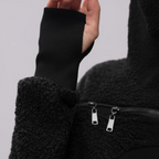 Close-up of a person wearing a black boucle fleece jacket with a blurred outdoor background