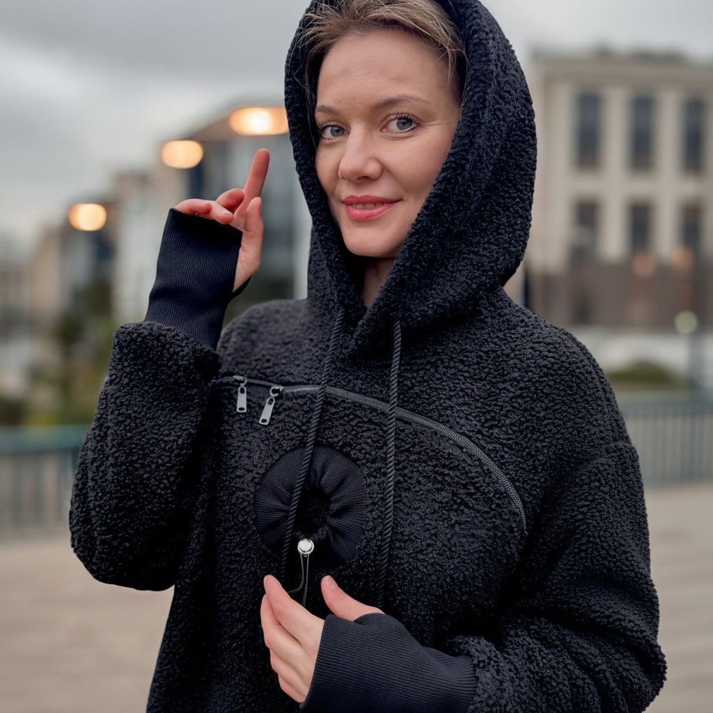 Woman wearing a black boucle  hooded coat in an outdoor setting with blurred lights in the background