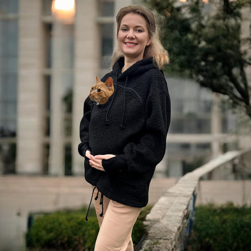 Woman wearing a black boucle hoodie with a cat peeking out, standing outdoors.