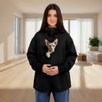 Person wearing a black sweatshirt with a Sphynx cat, standing indoors.