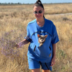 Woman in a blue t-shirt with a dog, holding a plant in a field