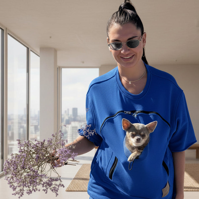 Person wearing a blue t-shirt with a dog in the pouch, holding flowers.