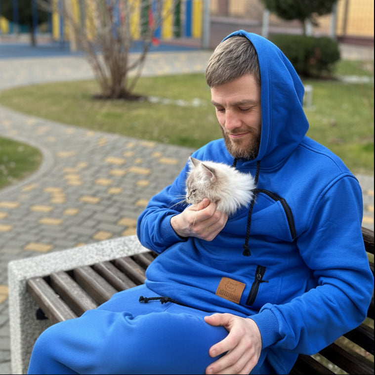 Man in a blue hoodie holding a cat on a bench outdoors