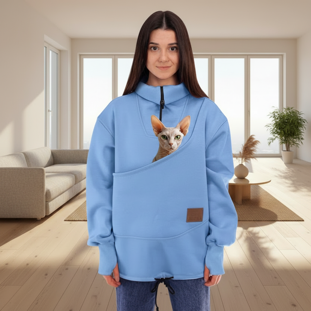 Women wearing a blue sweatshirt with a cat in the pouch, standing indoors.