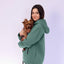 Woman wearing a emerald hoodie holding a small brown dog on a light purple background
