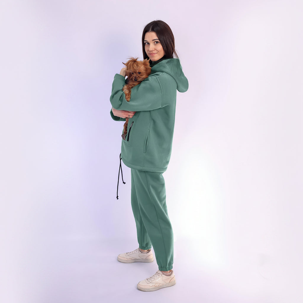 Woman in emerald  tracksuit holding a small dog on a white background