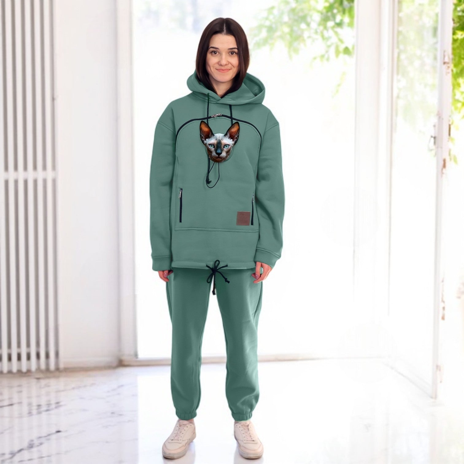 Person wearing a emerald hoodie and pants with a dog, standing in a bright room.