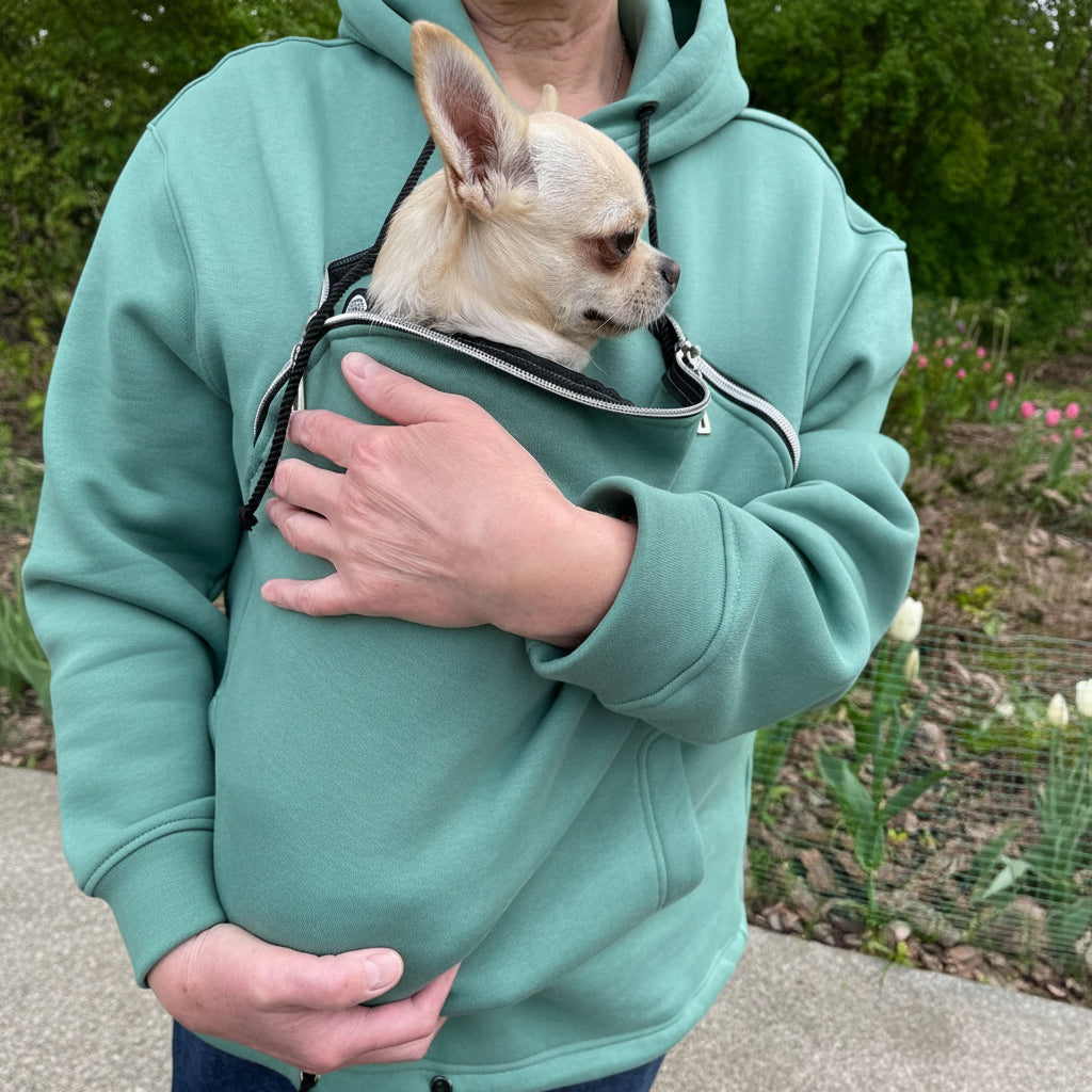Person wearing a emerald  hoodie holding a small dog in a matching pouch.