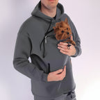 Person wearing a gray hoodie with a front pocket holding a small dog.