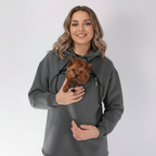 Woman wearing a gray hoodie with a pocket, holding a small brown dog.